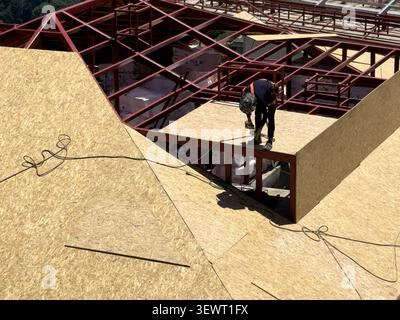 View of a construction worker installing wooden panels on a steel roof frame at a building site in Istanbul, Istanbul, Turkiye. Stock Photo