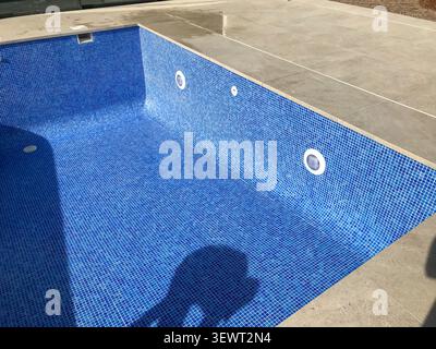 Empty outdoor swimming pool revealing blue mosaic tiles and steps, surrounded by stone paving on a sunny day during construction or renovation in cast Stock Photo