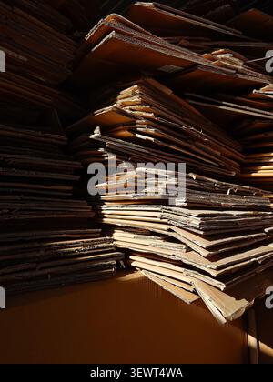 Large stacks of flattened cardboard boxes ready for recycling under warm sunlight. Stock Photo