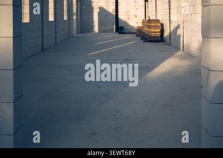 Sunlit unfinished concrete interior with cinder block walls and stacked wood on construction site, selective focus Stock Photo