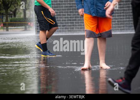 Children enjoy a public water fountain in an urban park. A refreshing and joyful outdoor summer scene Stock Photo