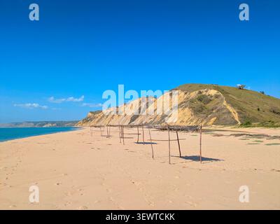 View of a sunny sandy beach at Cabo Ledo, Angola, with small ocean waves rolling onto the shore, a green rocky hill in the background, and a bright su Stock Photo