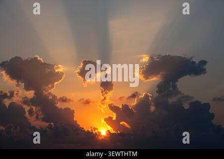 Sun setting behind dark clouds with dramatic golden crepuscular light rays Stock Photo