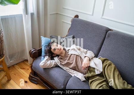 Bored thoughtful woman relaxing on sofa in room, laying staring at ceiling distracted by thoughts. Stock Photo