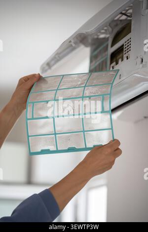 Woman removing dusty air conditioner coarse filter for washing, cleaning. Dust cause of illness Stock Photo