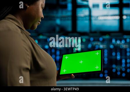 IT expert uses a green screen tablet in a data center for cloud service management, screen replacement, and server workflow monitoring. Stock Photo