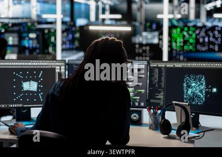 Woman programmer reviews an AI visualization dashboard on a PC in a server farm to find equipment issues and reduce hardware failures. Stock Photo
