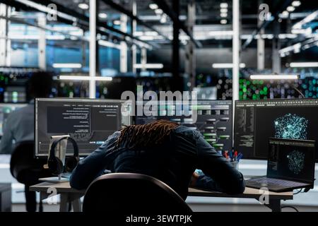 Exhausted data center engineer handles fatigue in a data center after a long hardware troubleshooting session at a computer workstation. Stock Photo