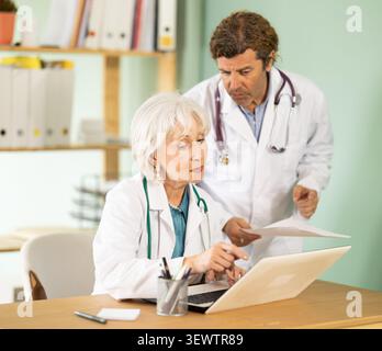 Senior woman and male doctors bent over laptop, work with medical soft Stock Photo