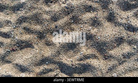 Close-up of natural beach sand texture with footprints and small pebbles Stock Photo