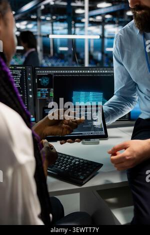 Data center programmers use a digital tablet in a data center to support automation monitoring and reliable server workflows. Stock Photo