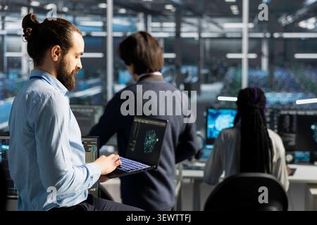 Data center engineer uses a laptop to manage AI training datasets and database workflows inside a server room. Stock Photo