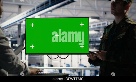 Soldier and female technician use a green screen computer in a server hub to manage systems with a mockup workstation. Stock Photo