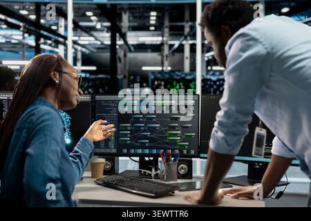 Manager supervises a technician coding in a server farm, overseeing repairs on data center racks used for computational operations. Stock Photo