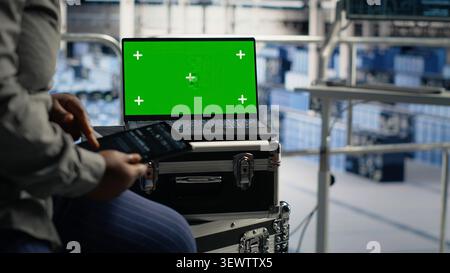 Data center worker uses a green screen tablet in a server room for AI workflow and screen replacement. Stock Photo
