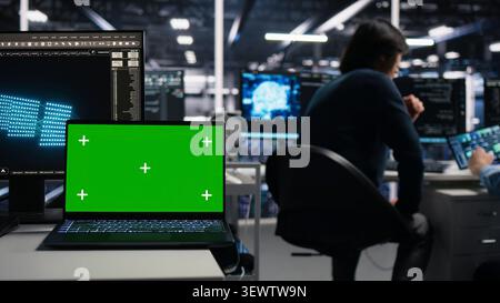 Software developer uses a green screen laptop to manage AI systems, machine learning workflows and server performance. Stock Photo