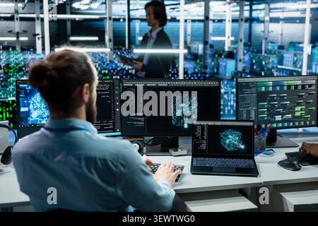 Software programmer working in high tech server room with hardware managing AI training datasets with IT staff member overseeing machine learning tech in server facility supporting scalable digital. Stock Photo