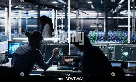 Senior programmer and coworker programs on a computer workstation in a data center with generative AI assistance. Stock Photo