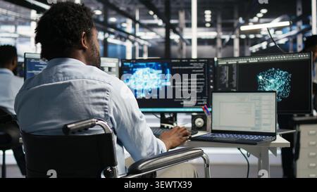Computing hub software programmer with paraplegia in wheelchair operates AI machine learning visual programming system with man with disability in inclusive server facility assesses equipment issues. Stock Photo