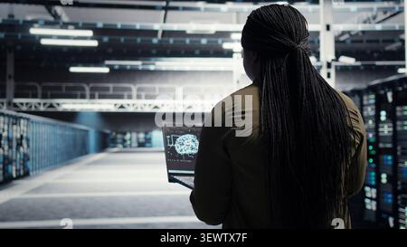 Software developer uses laptop-based deep learning tools in a server room to improve AI operations and system efficiency. Stock Photo