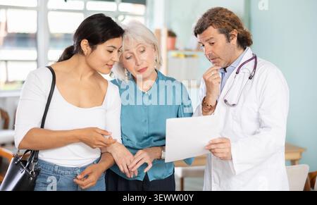 Happy elderly woman with daughter discussing medical tests with doctor Stock Photo