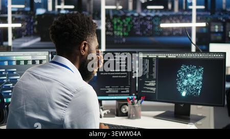 Data infrastructure center computer scientist interprets AI generated data analytics graphs, while african american man in server facility working with AI program showing predictive system metrics. Stock Photo