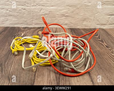 A disorganized pile of orange yellow and white ethernet cables with connectors on a wood grain floor surface Stock Photo