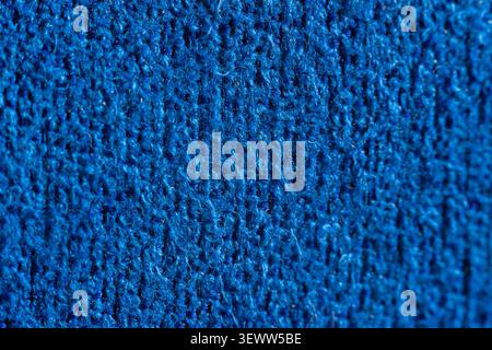 Deep blue knitted fabric fills the frame. Texture shows rows of interlocking stitches. Close-up view highlights yarn's fine details. Soft, uniform col Stock Photo