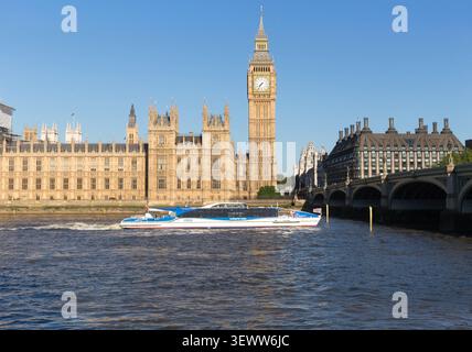 An MBNA Thames Clippers boat cruises the River Thames past the Palace of Westminster and Big Ben, providing scenic transit through London. Stock Photo