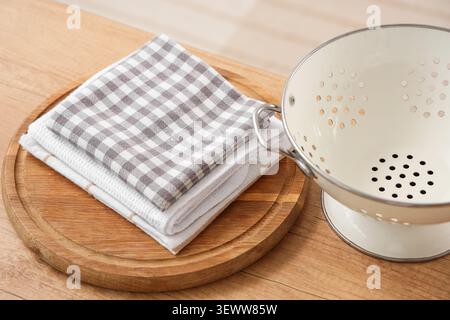 Stack of kitchen towels and white colander on wooden table Stock Photo