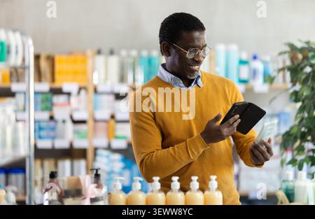 Male customer using smartphone to choose skincare product in pharmacy Stock Photo