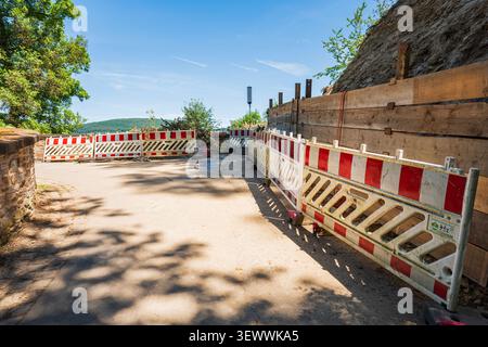 Road construction site with red and white safety barriers and wooden retaining wall for landslide protection on a sunny day Stock Photo