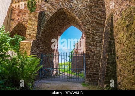 Ancient stone arch with medieval iron gate in fortress wall under blue sky Stock Photo