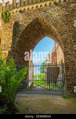 Ancient stone arch with medieval iron gate in fortress wall under blue sky Stock Photo
