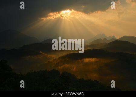 Dramatic Sunbeams Breaking Through Dark Clouds Over Misty Mountain Landscape Stock Photo