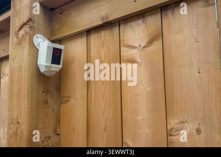 modern outdoor security camera mounted on a wooden fence. Home surveillance, property protection, smart security and residential safety concept. Stock Photo