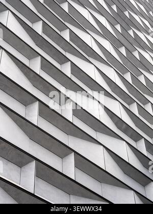 Modern architectural facade with geometric metal panels forming an abstract pattern. Contemporary building exterior featuring angular lines, texture, Stock Photo