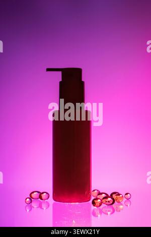 Dark silhouette of bottle with dispenser, gradient purple-pink neon background, with transparent golden capsules reflected on glossy surface Stock Photo