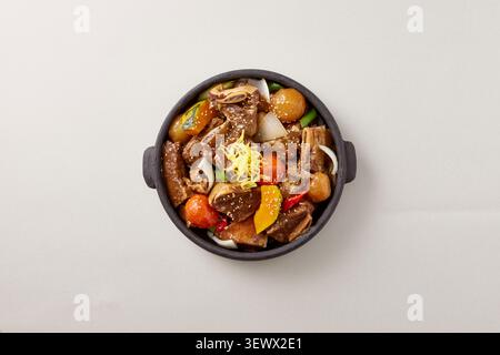 Korean spicy seafood and braised meat hot pot served in a black earthenware pot with crab, abalone and vegetables on a light gray background Stock Photo
