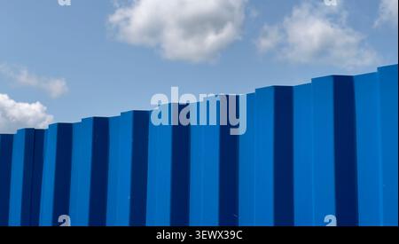 Blue corrugated metal fence forming repetitive geometric pattern against sky. Minimal architectural texture showing vertical lines and industrial desi Stock Photo