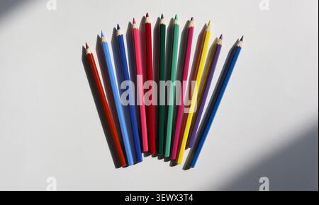 A group of colored pencils is placed on a white surface. The pencils are lined up with their tips facing up. Different colors are visible, showing a r Stock Photo