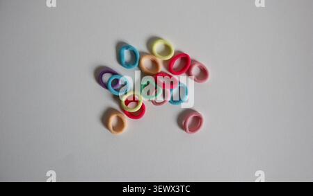 Small rubber bands in various colors are arranged on a white surface. They can be used for organizing items or in crafts. The bands vary in shape and Stock Photo