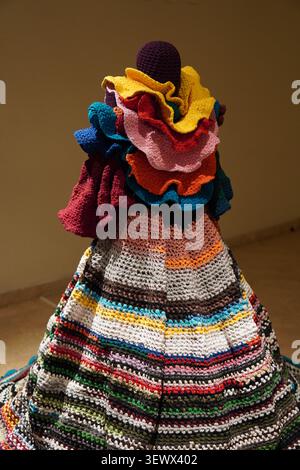 Unique colorful crochet art installation shaped like a dress with vibrant layered ruffles on display inside a gallery museum. Stock Photo