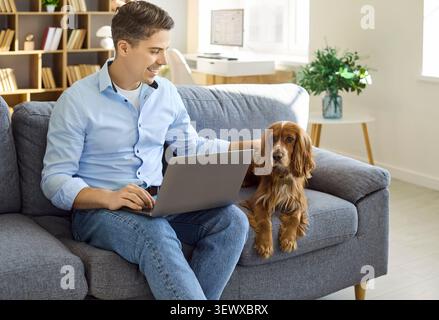 Man working from home on sofa with laptop and cocker spaniel dog, cozy lifestyle Stock Photo