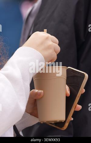 Close-up of hands holding a reusable eco-friendly cup and a smartphone at the Naplavka farmers market in Prague. Modern urban lifestyle, sustainable c Stock Photo