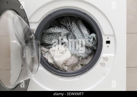 Close-up of open washing machine drum with laundry inside, household cleaning concept Stock Photo