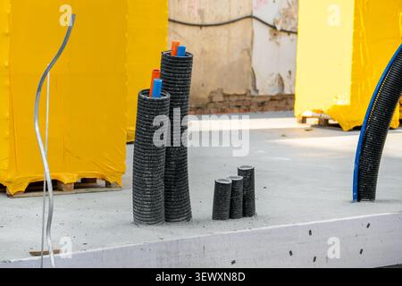 Corrugated conduit ducts colored utility pipes emerge concrete foundation active construction site. Infrastructure installation shows preparation for Stock Photo
