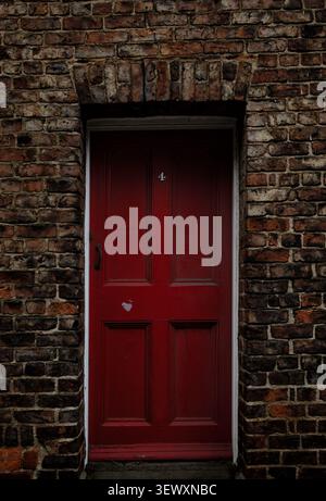 A simple, striking composition of a bright red door numbered "4," set into a textured, historic weathered brick wall in Durham Stock Photo