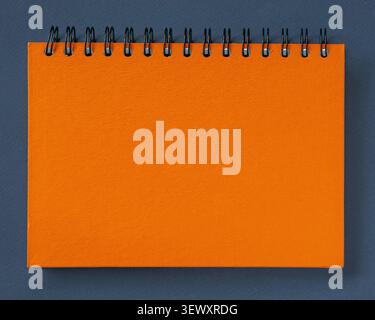 Orange spiral notebook cover on dark paper backdrop with metal binding and empty layout. Notebook planning, notebook mockup, stationery branding Stock Photo