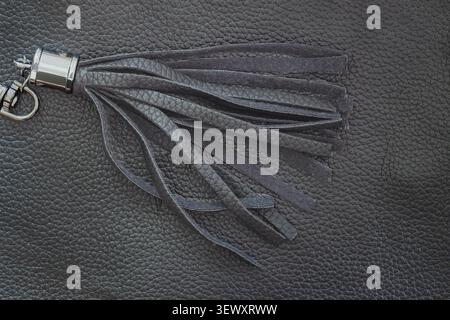 Leather tassel with metal ring on leather texture, copy space for accessory design. Close up of leather tassel, bag charm, fashion accessory detail Stock Photo